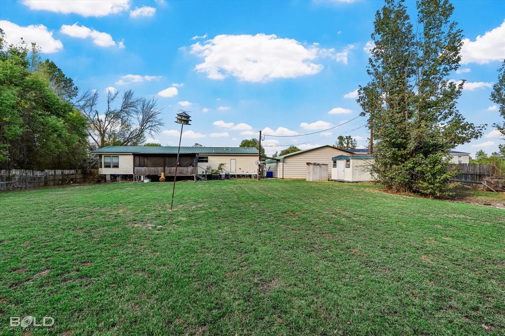 Expansive backyard featuring a grass lawn, metal-roofed covered porch, detached storage building, and perimeter fencing