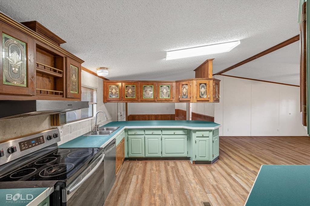 Kitchen featuring wood-finish flooring, ample cabinetry with decorative glass inserts, solid-surface countertops, stainless steel appliances, and a double-basin sink
