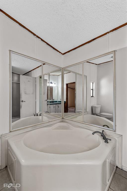 Corner soaking tub featuring a tiled surround, mirrored wall panels, and metal faucet fixtures