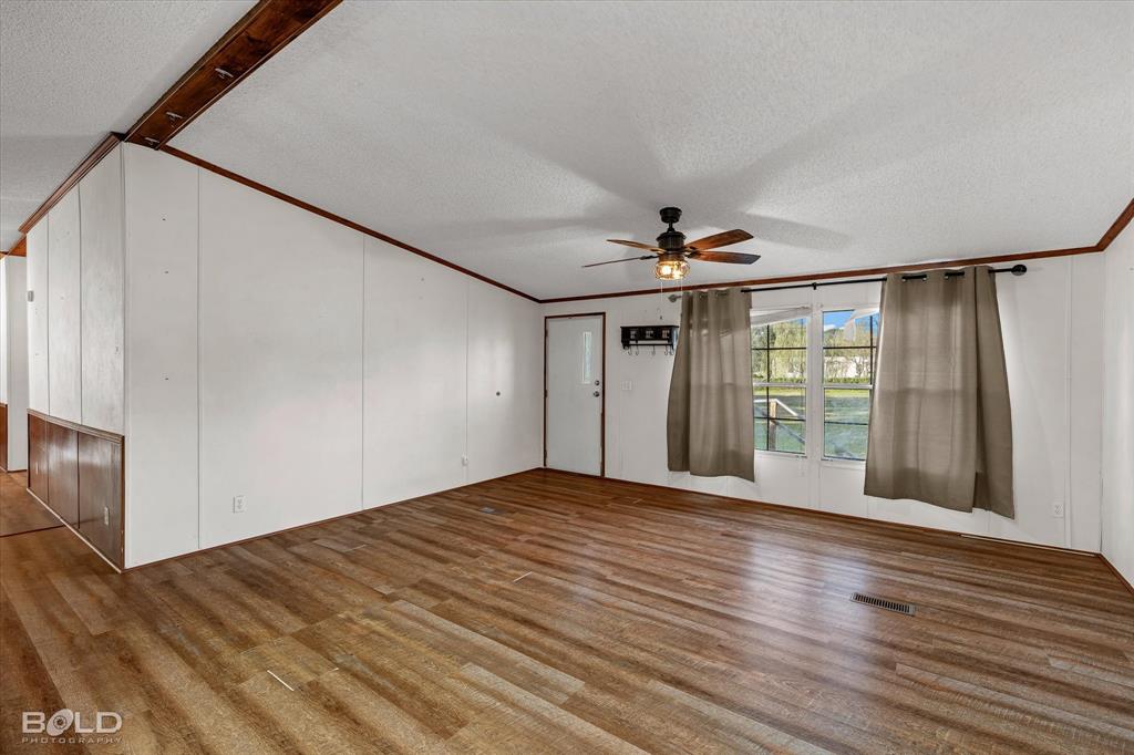 Wood-finish flooring, white paneled walls, wood-trimmed ceiling beams, and a ceiling fan with integrated lighting
