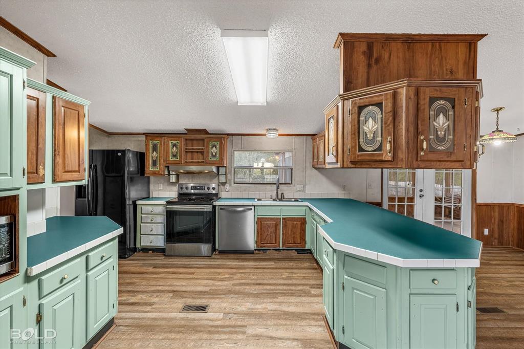 Kitchen featuring wood-finish flooring, solid-surface countertops, custom two-tone cabinetry with glass-panel inserts, stainless steel appliances, and French doors