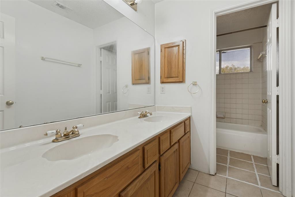 Dual-sink vanity with a solid-surface countertop, full-width wall mirror, wood cabinetry, and a tile-surround bathtub Dual-sink vanity with a solid-surface countertop, full-width wall mirror, wood cabinetry, and a tile-surround bathtub