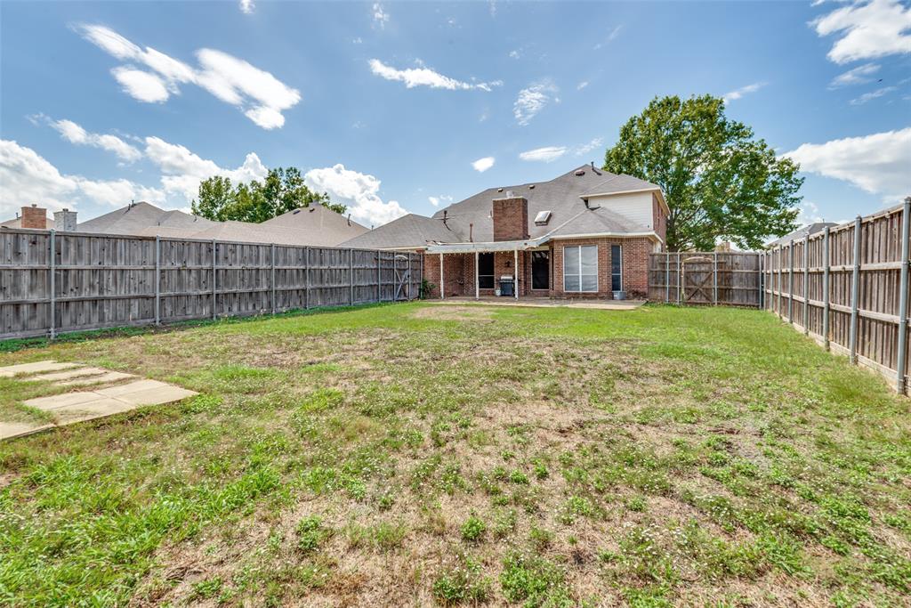 Rear exterior featuring a brick facade, covered patio, masonry chimney, and full-height wood fencing