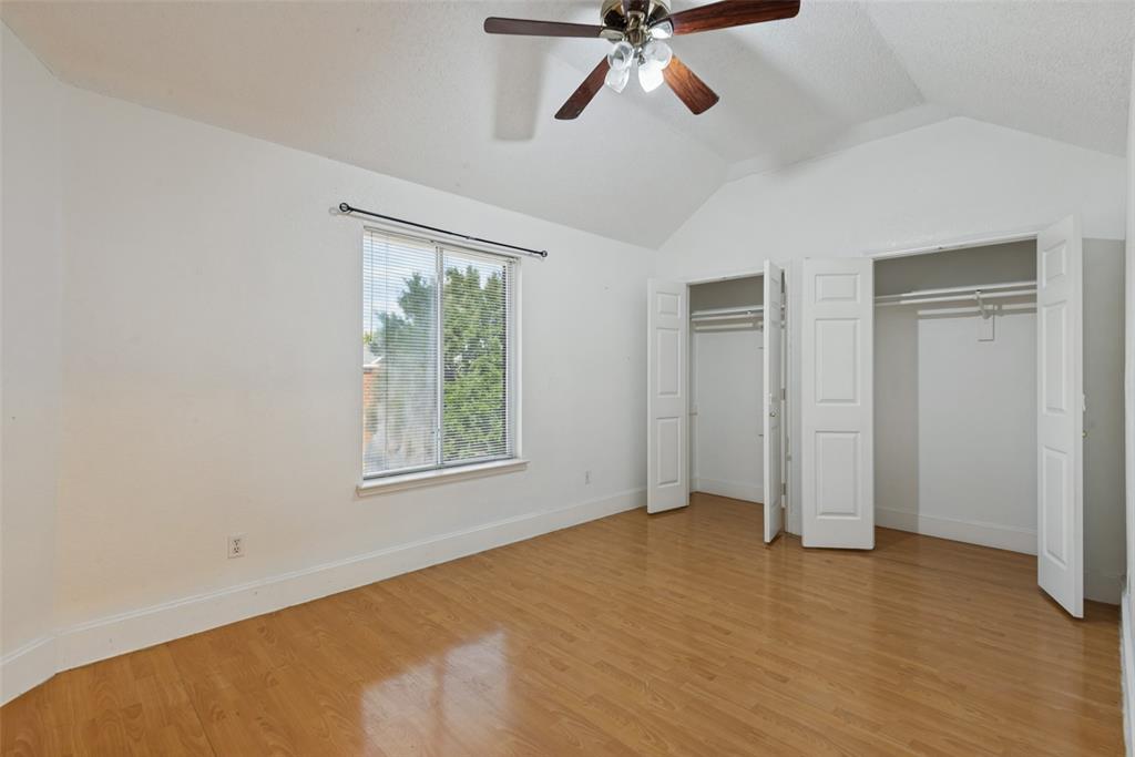 Vaulted ceiling with integrated multi-light ceiling fan, wood-finish flooring, dual closets with panel doors, and window with horizontal blinds Vaulted ceiling with integrated multi-light ceiling fan, wood-finish flooring, dual closets with panel doors, and window with horizontal blinds