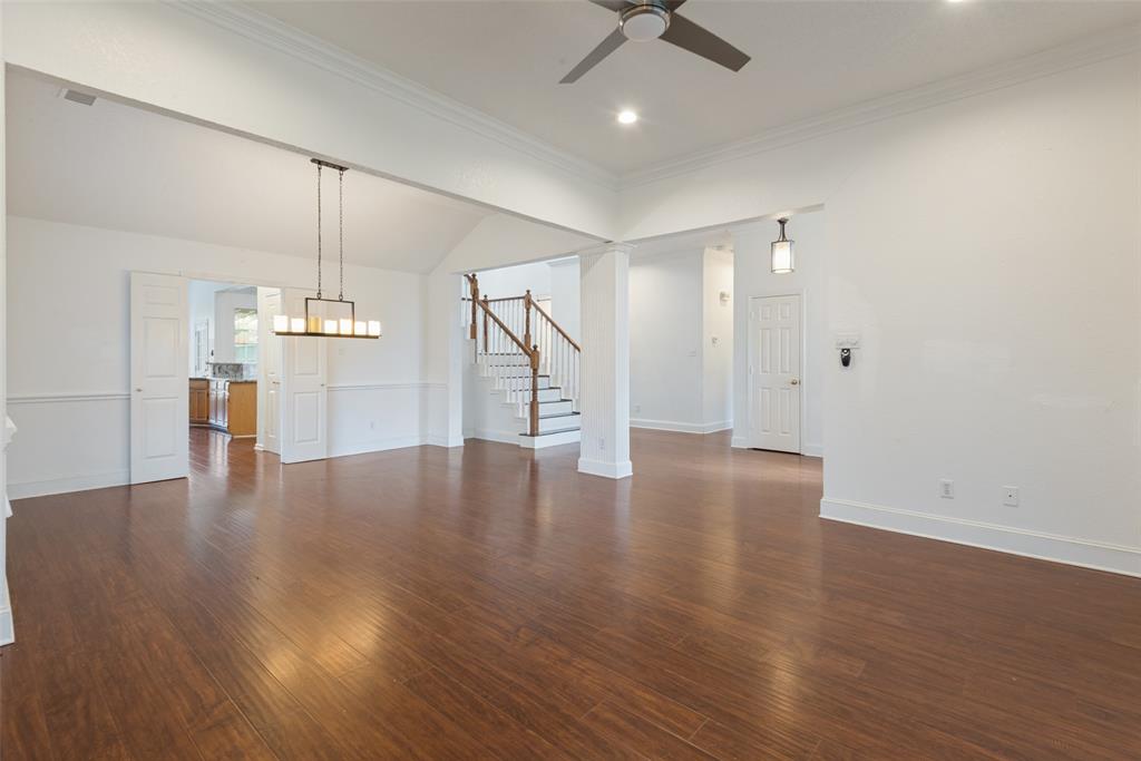 Open interior space featuring wood-finish flooring, vaulted ceilings, crown molding, a multi-light pendant fixture, and a staircase with a wooden handrail Open interior space featuring wood-finish flooring, vaulted ceilings, crown molding, a multi-light pendant fixture, and a staircase with a wooden handrail