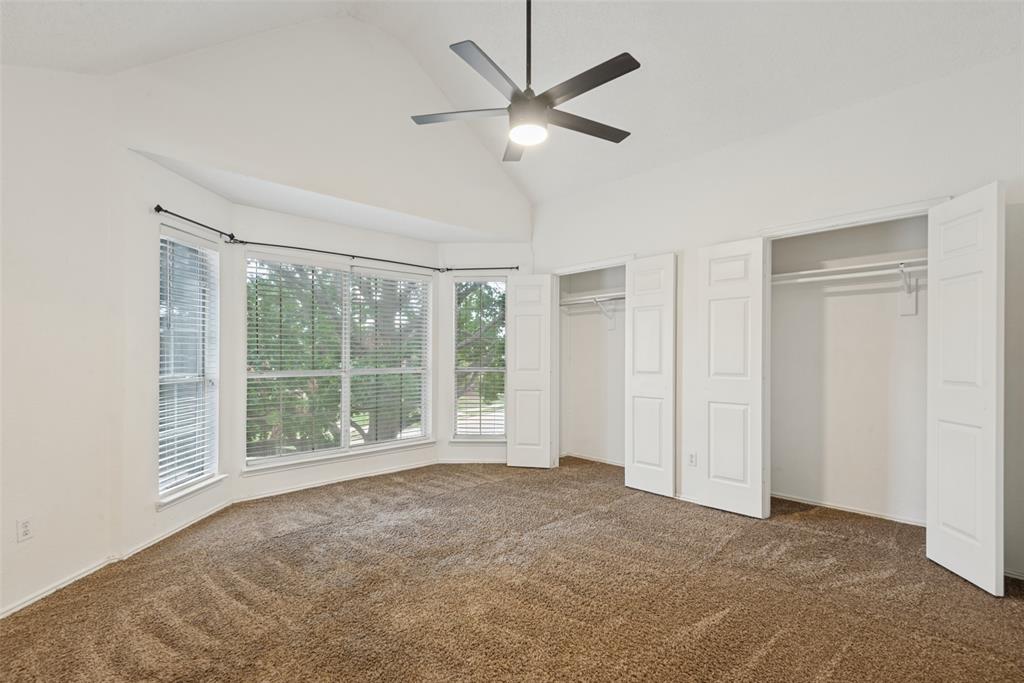 Vaulted ceilings with a central matte black ceiling fan, expansive bay window, and dual closets featuring white paneled doors Vaulted ceilings with a central matte black ceiling fan, expansive bay window, and dual closets featuring white paneled doors