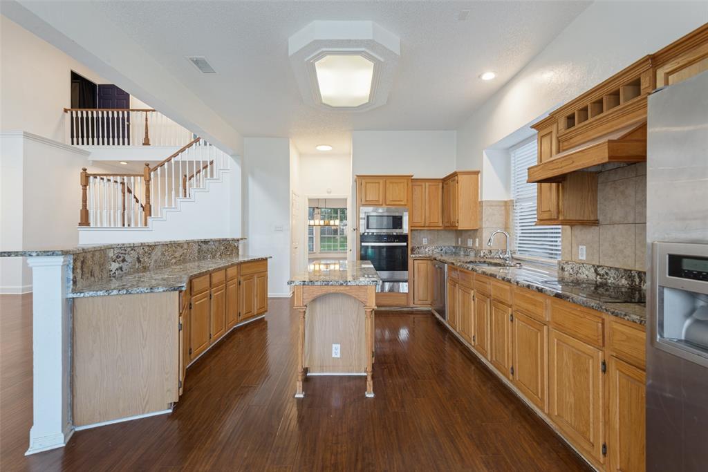 Kitchen featuring wood cabinetry, stone countertops, a center island, stainless steel appliances, and dark wood-finish flooring Kitchen featuring wood cabinetry, stone countertops, a center island, stainless steel appliances, and dark wood-finish flooring