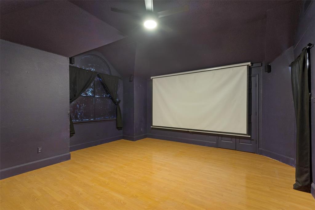 Vaulted ceilings with an integrated ceiling fan, wood-finish flooring, and a mounted projection screen