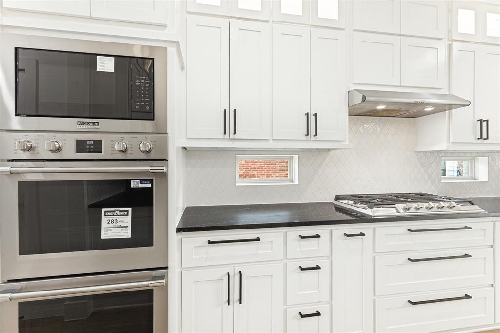Kitchen featuring shaker-style white cabinetry, dark stone countertops, stainless steel wall-mounted oven and microwave, gas cooktop, and herringbone-patterned tile backsplash