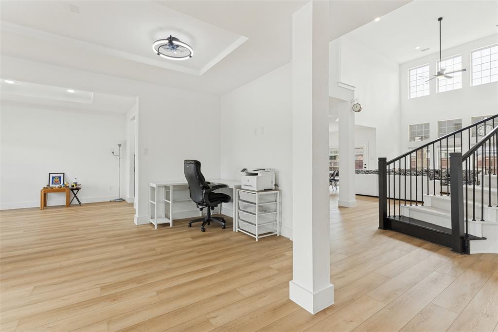 Open-concept floor plan featuring wood-finish flooring, recessed lighting, double-height ceilings, and a staircase with a black metal railing