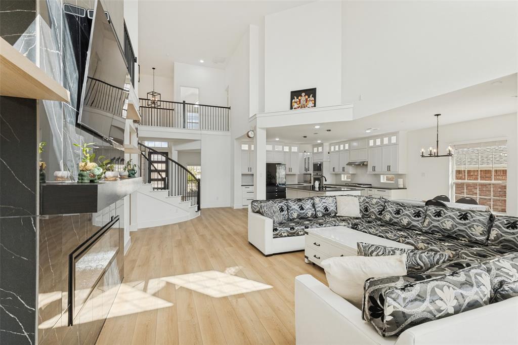 Double-height ceilings featuring a focal fireplace with full-height stone-finish surround, wood-finish flooring, and a curved staircase with iron balusters