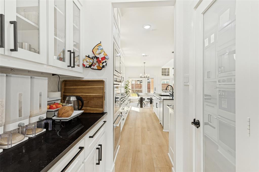 Kitchen butler's pantry featuring white cabinetry with glass-front uppers, dark stone-finish countertops, wood-finish flooring, and a walk-in pantry with a frosted glass door