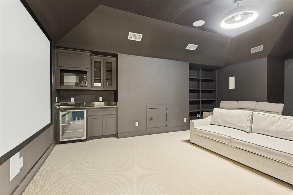 Media room featuring a fixed projection screen, built-in cabinetry with stone countertops, a glass-front beverage refrigerator, integrated shelving, and recessed ceiling lighting