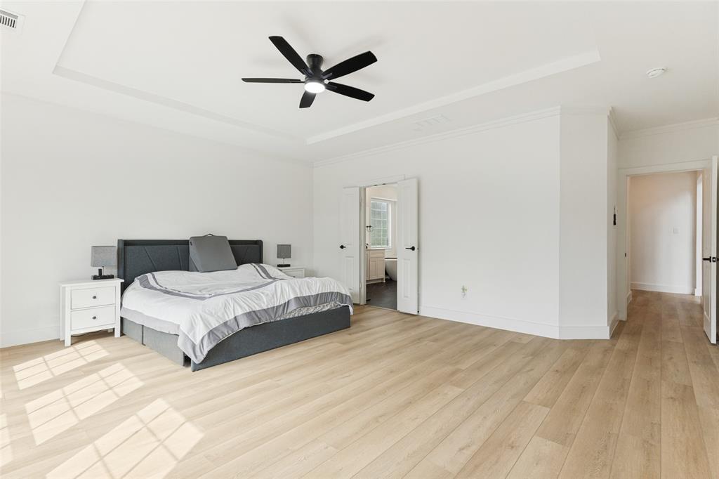 Tray ceiling with a central matte black ceiling fan, wood-finish flooring, and double-door entry