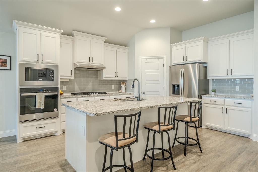 Kitchen featuring white cabinetry, stone-surface central island, subway tile backsplash, stainless steel built-in oven and microwave, and wood-finish flooring