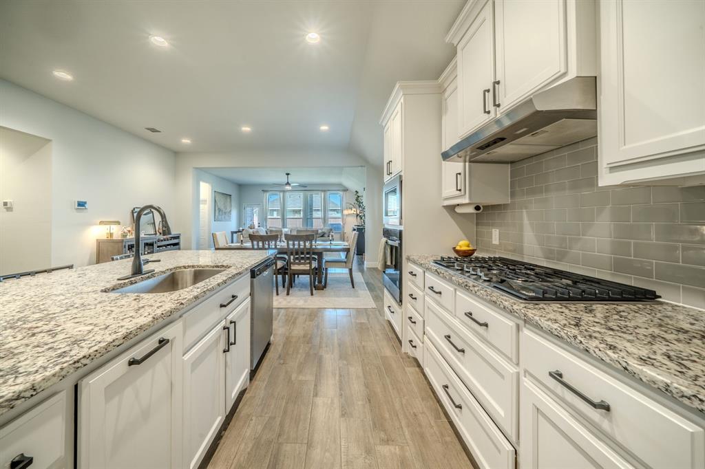Kitchen featuring white shaker-style cabinetry, stone countertops, a subway tile backsplash, built-in stainless steel double ovens, and wood-finish flooring