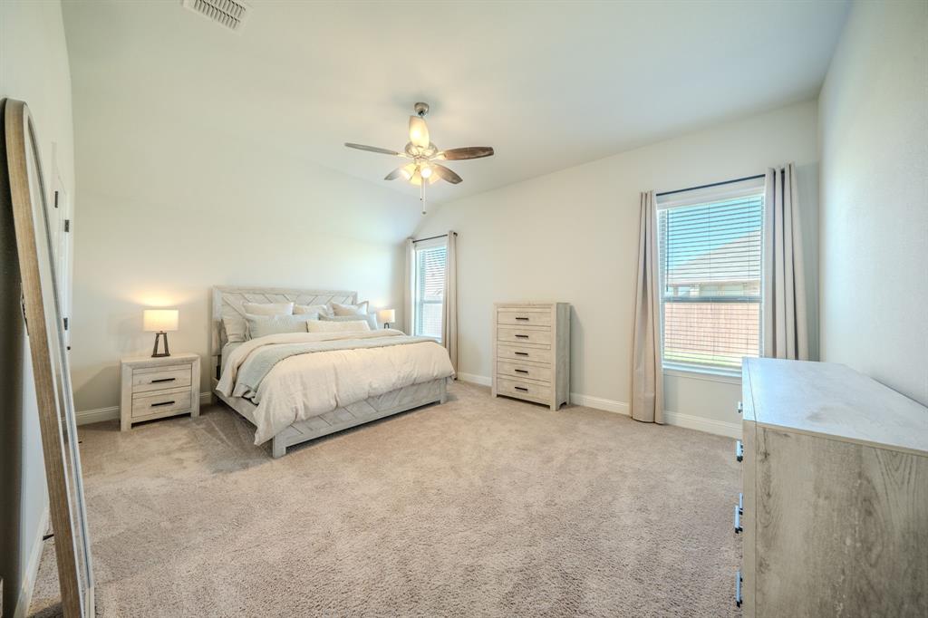 Bedroom featuring a vaulted ceiling, neutral wall-to-wall carpeting, dual windows, and a ceiling fan with integrated lighting