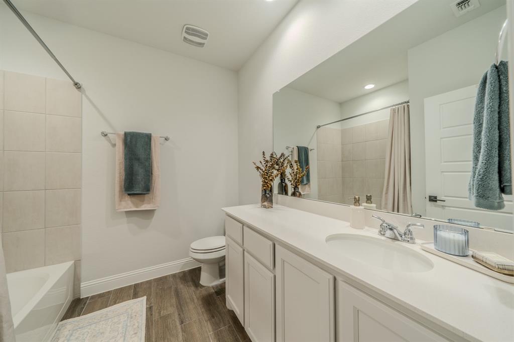 Full-width vanity with solid-surface countertop, integrated oval sink, chrome dual-handle faucet, large vanity mirror, and wood-finish flooring