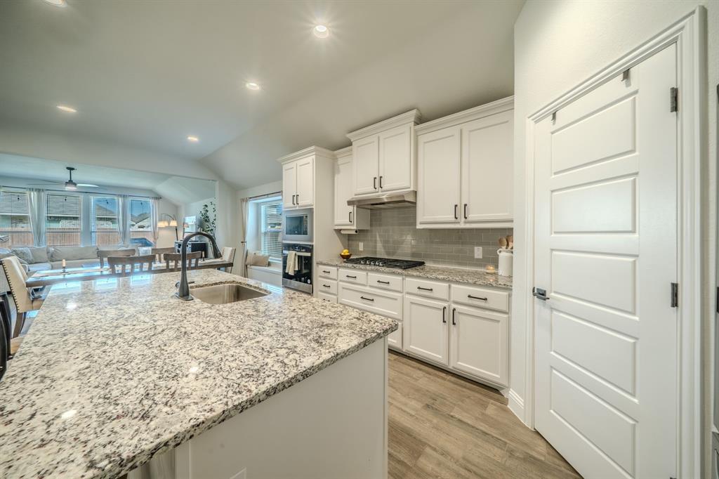 Kitchen featuring a central island with a stone-finish countertop and undermount sink, white cabinetry, a built-in oven, a gas cooktop, and wood-finish flooring