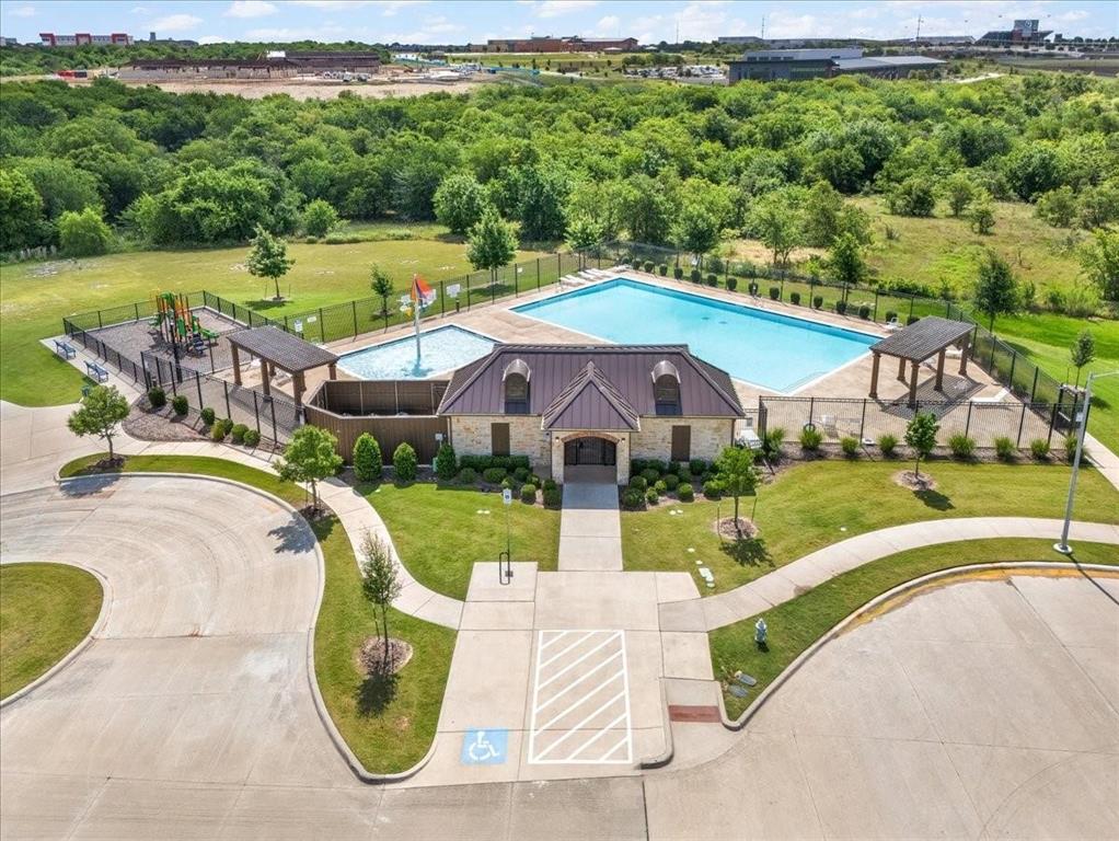 Community recreation area featuring a swimming pool, shallow splash pad with water feature, covered cabana structures, and a playground enclosure