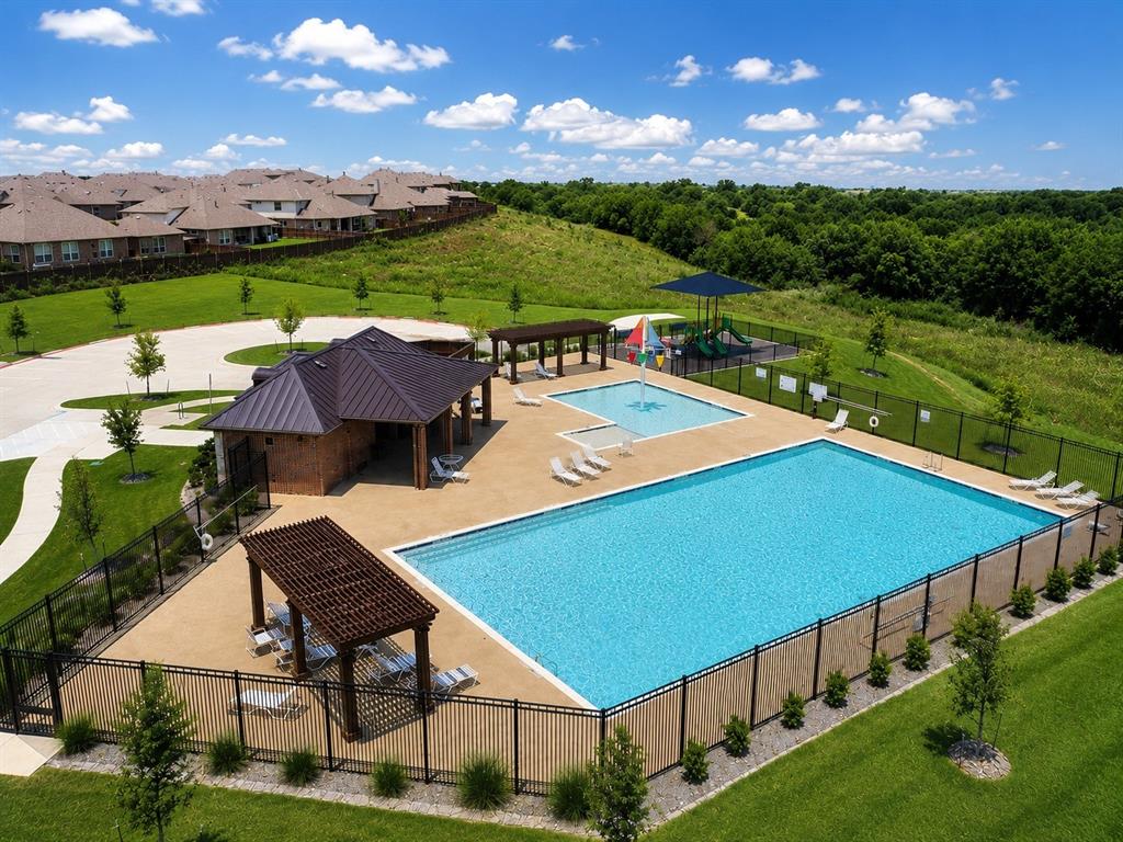 Community swimming pool featuring a lap pool, a shallow-entry pool with a water feature, a covered pavilion with a metal roof, and wood-beam pergolas, all enclosed by decorative metal fencing