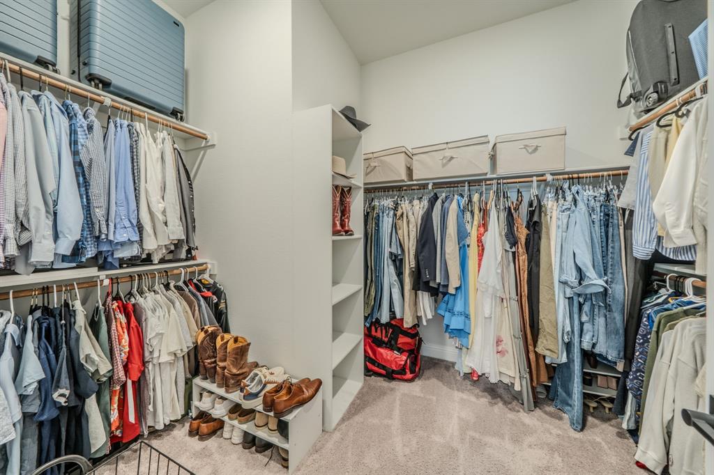 Walk-in closet featuring tiered shelving, built-in vertical storage tower, dual-level hanging rods, and neutral carpeting