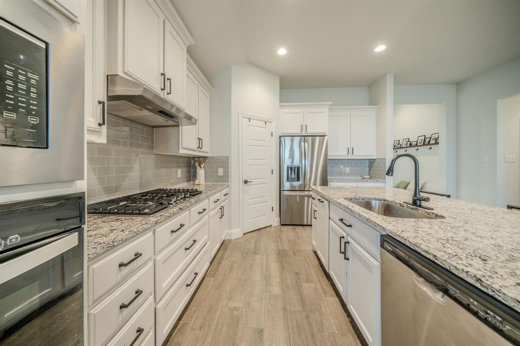 Kitchen featuring white shaker-style cabinetry, stone countertops, stainless steel appliances, a grey subway tile backsplash, and wood-finish flooring