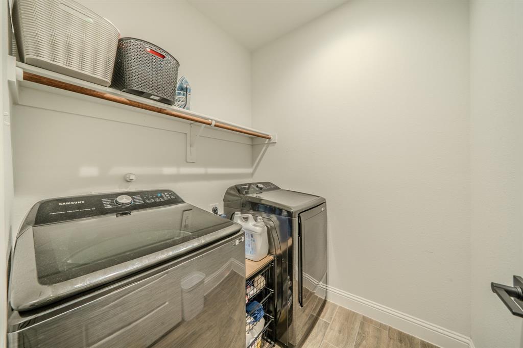 Laundry space featuring wood-finish flooring, a wall-mounted shelving unit with an integrated hanging rod, and neutral wall tones