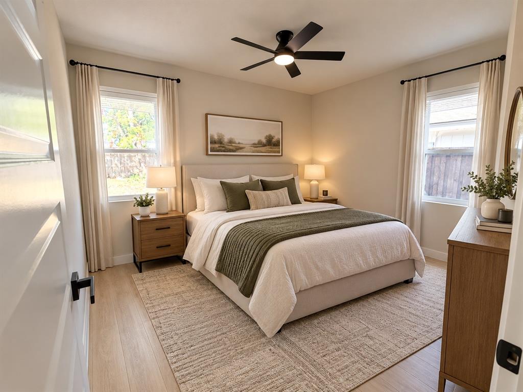 Neutral interior space featuring wood-finish flooring, dual windows with black hardware, and a ceiling-mounted light fixture with fan blades