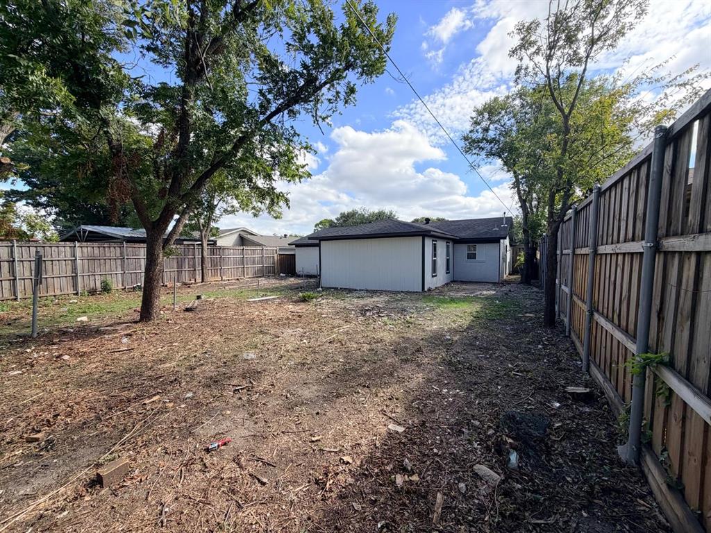 Rear yard featuring vertical siding exterior, wood privacy fencing, and mature trees
