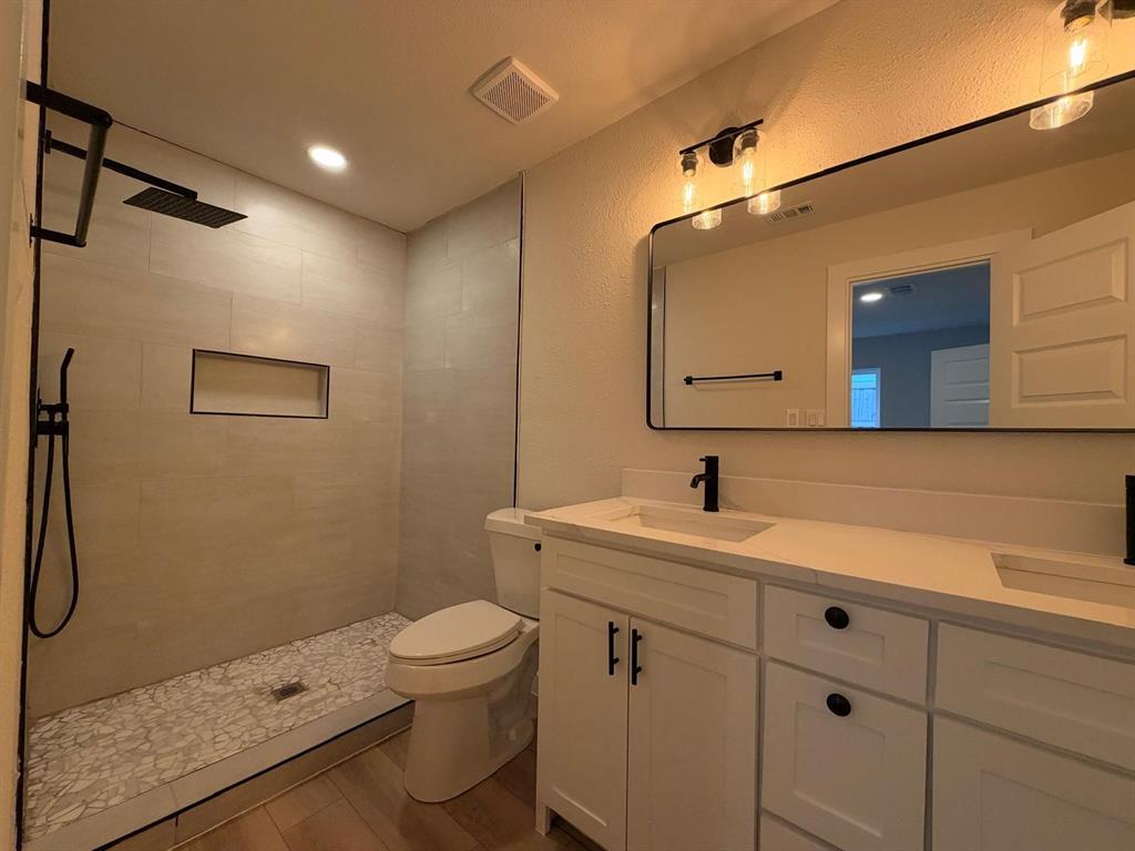 Double vanity with light-toned countertops, matte black plumbing fixtures, walk-in shower with tiled surround and built-in niche, and oversized vanity mirror with integrated lighting