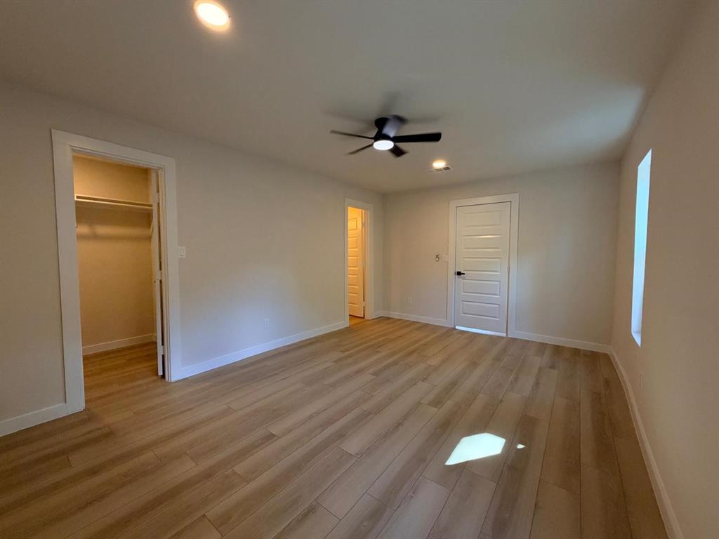 Neutral-toned room featuring wood-finish flooring, a multi-panel interior door, recessed lighting, and a ceiling fan with integrated light