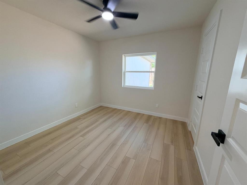 Interior room featuring wood-finish flooring, a matte black ceiling fan with integrated lighting, a single-hung window, and a paneled door with matte black hardware