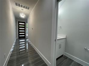 Entry hallway featuring wood-finish flooring, a contemporary crystal-accented chandelier, and a modern six-panel door with glass inserts, accompanied by a powder room containing a white built-in vanity with a square sink