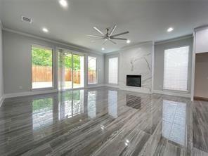 Large living space featuring high-gloss, linear-patterned tile flooring, a floor-to-ceiling stone fireplace surround, oversized sliding glass doors, a multi-blade ceiling fan, and recessed lighting