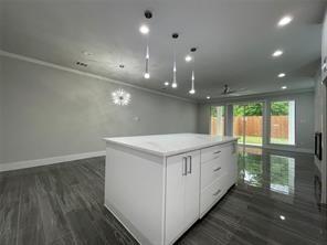 Kitchen island featuring a white stone-surface countertop, white cabinetry with silver-tone hardware, recessed ceiling lighting, three suspended pendant lights, and wood-finish flooring