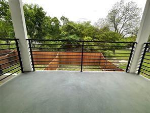 Covered balcony featuring concrete flooring, structural support columns, and black horizontal metal railings overlooking a fenced backyard