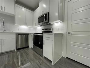 Kitchen featuring white cabinetry, stainless steel appliances, wood-finish flooring, and a subway tile backsplash