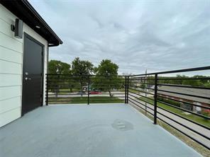 Elevated deck featuring horizontal black metal railings, a solid-surface floor, a black entry door, and wall-mounted exterior lighting
