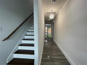 Staircase featuring dark-stained wood treads and white risers with a matching handrail, complemented by grey wood-finish flooring, a modern multi-light chandelier, and glass-paneled entry door