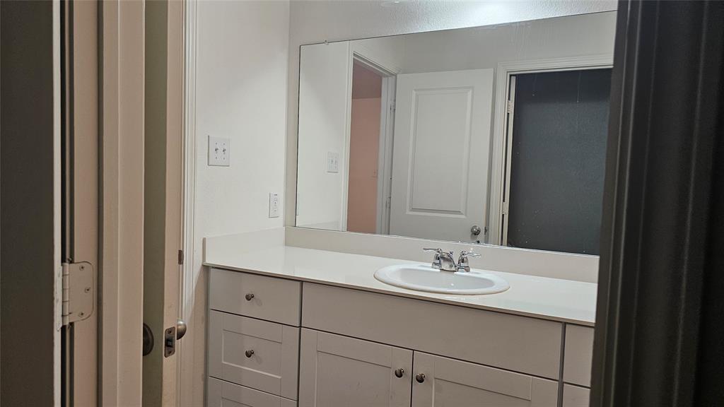Bathroom vanity featuring a solid surface countertop, integrated oval sink, chrome dual-handle faucet, white Shaker-style cabinetry, and a large wall-mounted mirror