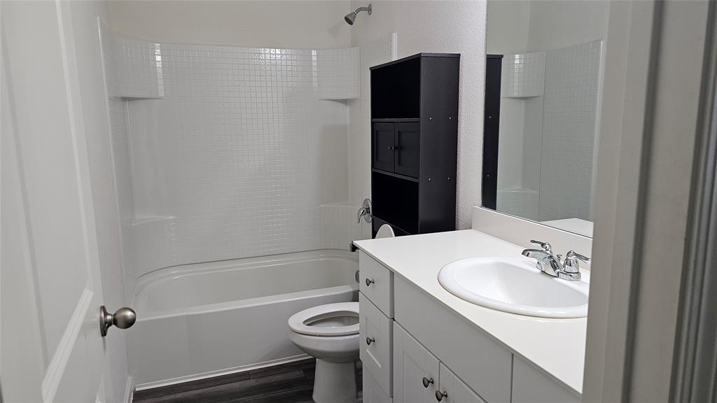 Bathroom featuring a tub-shower combination with tiled surround, vanity with an integrated basin, chrome-finish faucet, and wood-finish flooring