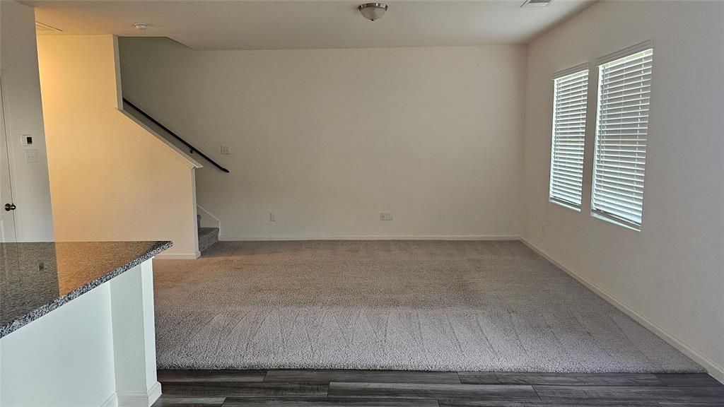 Interior area featuring carpeting, wood-finish flooring, a stairway with a black railing, and windows with horizontal blinds Interior area featuring carpeting, wood-finish flooring, a stairway with a black railing, and windows with horizontal blinds