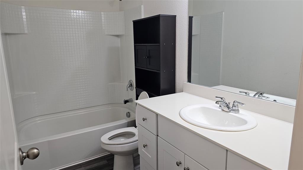 Bathroom featuring a vanity with a solid-surface countertop and integrated basin, chrome-finish dual-handle faucet, oversized wall-mounted mirror, and a tub-shower combination with a grid-pattern surround