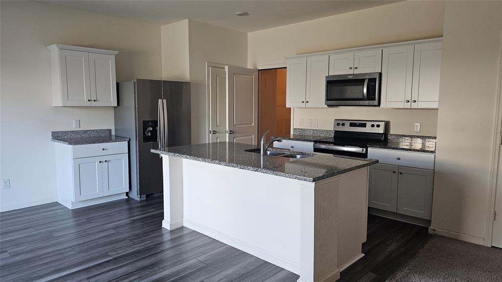 Kitchen featuring a central island with a stone-finish countertop, white cabinetry, stainless steel appliances, and wood-finish flooring Kitchen featuring a central island with a stone-finish countertop, white cabinetry, stainless steel appliances, and wood-finish flooring
