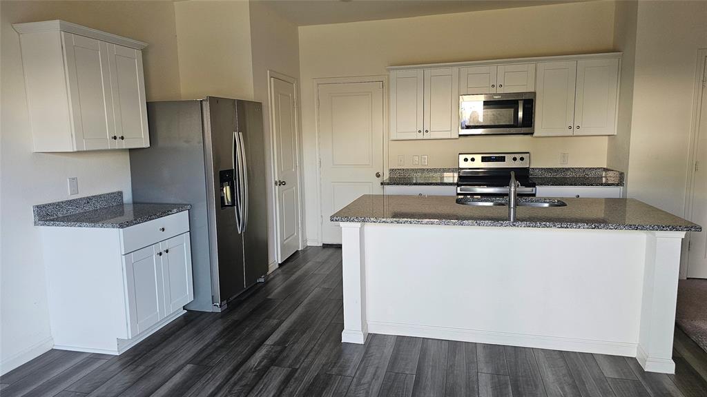 Kitchen featuring white shaker-style cabinetry, speckled stone-finish countertops, stainless steel appliances, a center island with a dual-basin sink, and wood-finish flooring Kitchen featuring white shaker-style cabinetry, speckled stone-finish countertops, stainless steel appliances, a center island with a dual-basin sink, and wood-finish flooring