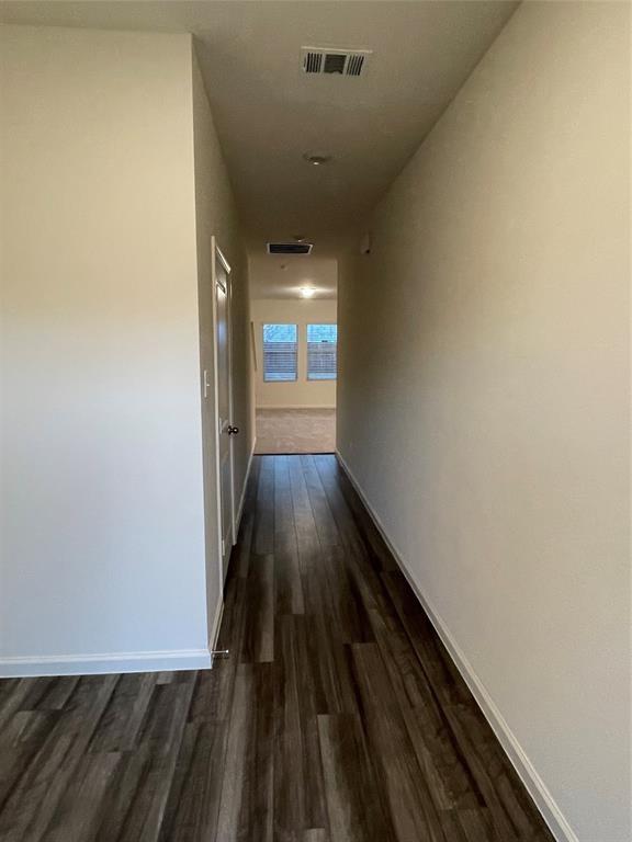 Hallway featuring neutral wall tones and dark wood-finish flooring Hallway featuring neutral wall tones and dark wood-finish flooring