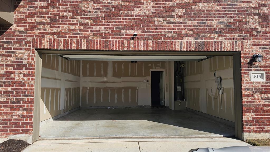 Attached two-car garage featuring red brick exterior, concrete flooring, and an integrated water heater Attached two-car garage featuring red brick exterior, concrete flooring, and an integrated water heater