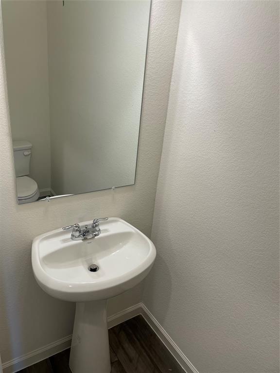 White pedestal sink with a dual-handle chrome faucet, large rectangular wall-mounted mirror, white ceramic toilet, and wood-finish flooring