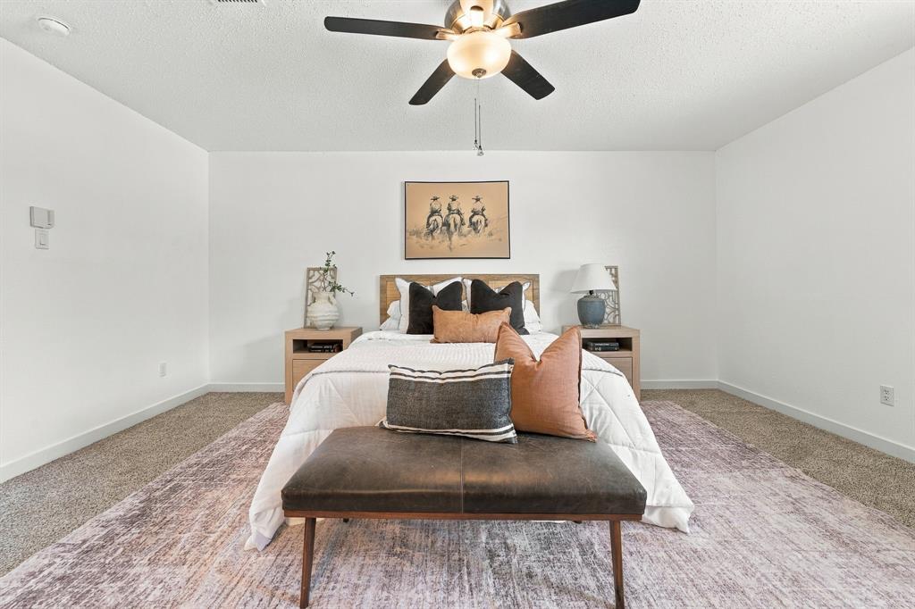 Neutral-toned carpeted flooring, textured ceiling, and centrally-mounted multi-blade ceiling fan with integrated lighting